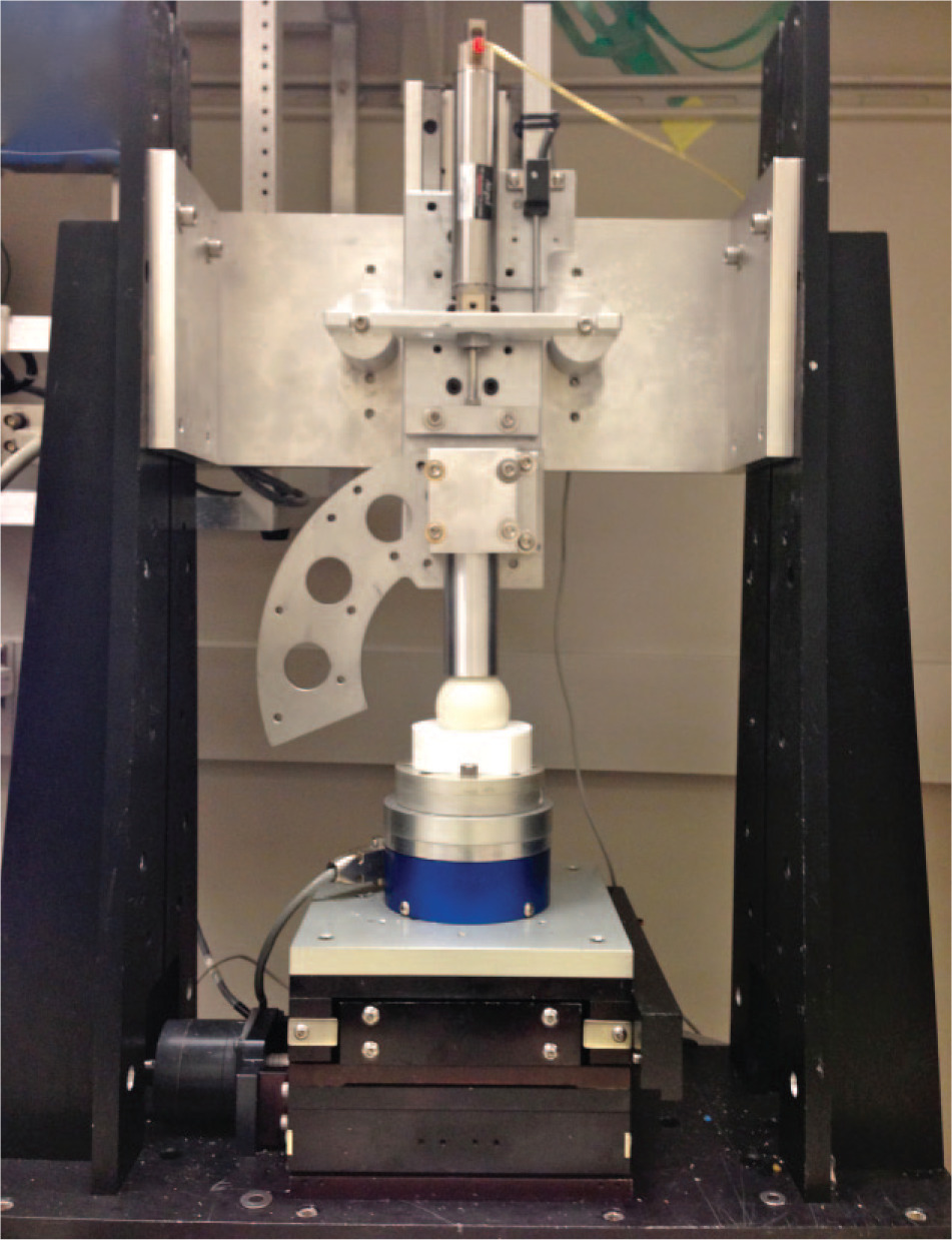 Fig. 1 
            A photograph of the custom testing machine and the experimental setup. The high density polyethylene plastic ball is mounted on an aluminium rod, whereas the moulded socket is mounted on an aluminium plate attached to the load cell (blue).
          